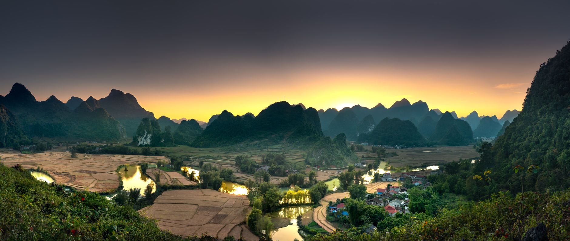 A breathtaking sunrise over a valley with farmlands and picturesque mountains.