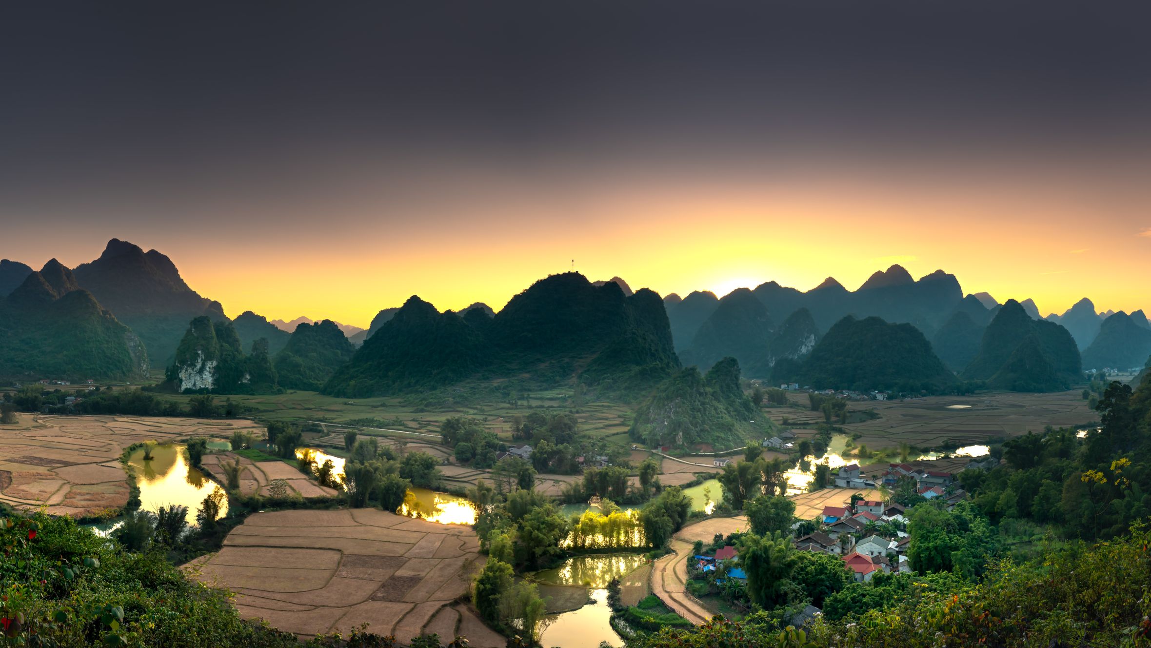 A breathtaking sunrise over a valley with farmlands and picturesque mountains.