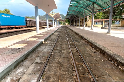 Deserted railway platform at a station with cargo containers visible under clear sky.