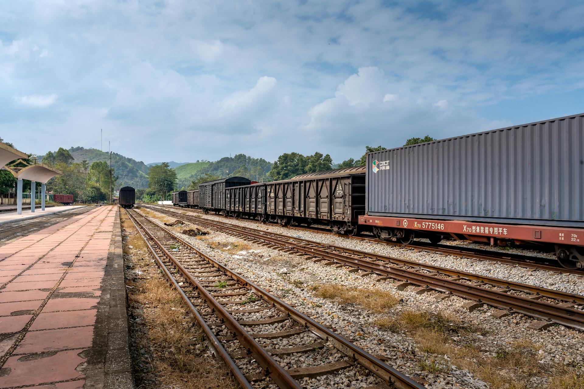 Cargo train with containers and tracks in a sunny outdoor railway setting.