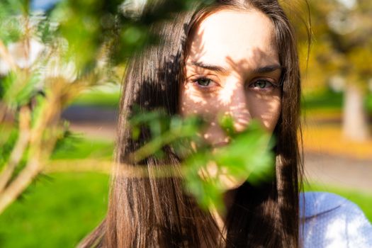 Portrait of a young woman with sunlight and leaf shadows outdoors.