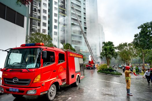 Firefighters extinguishing smoke from a building with fire trucks in an urban area.