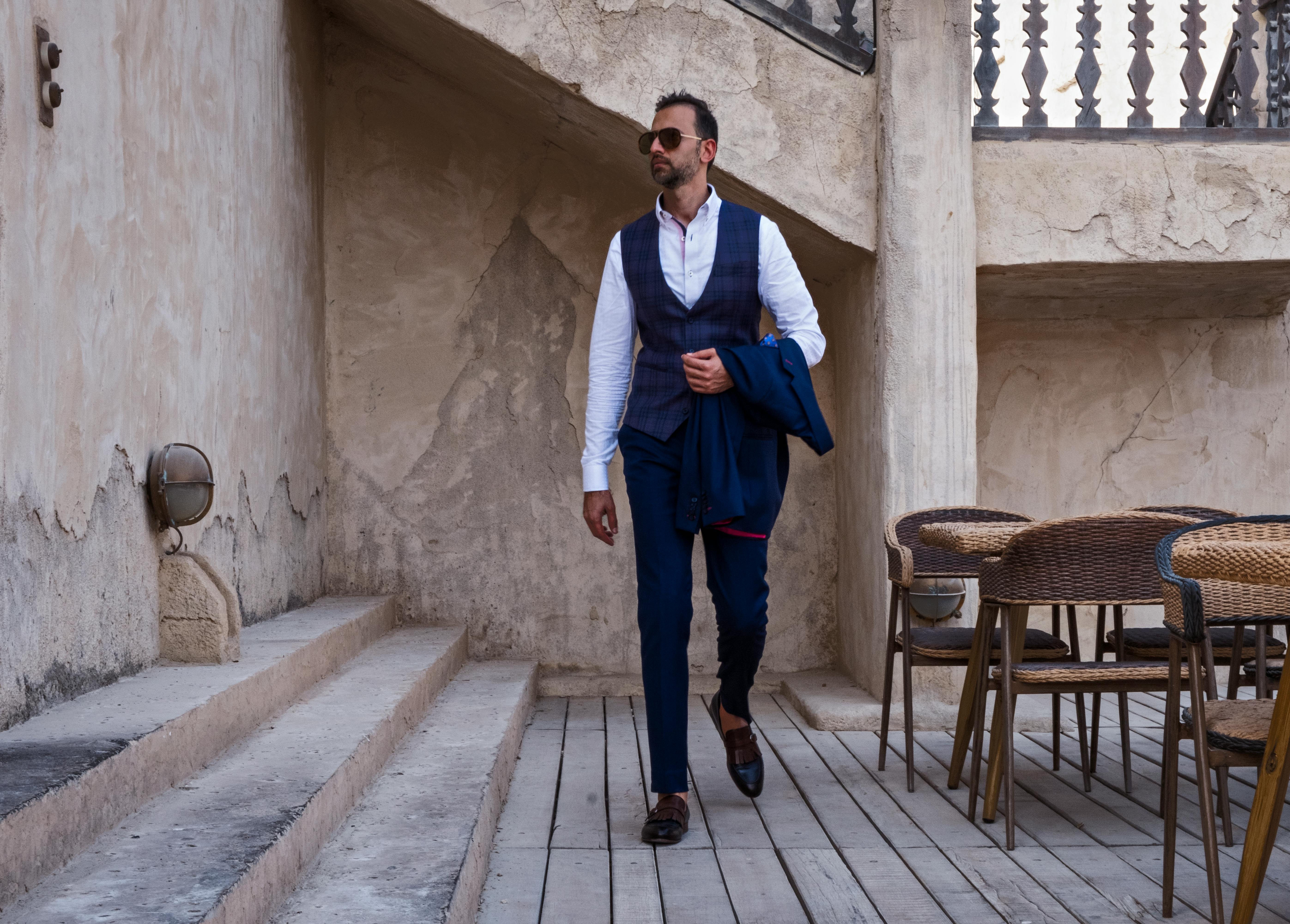 一位时尚男子穿着时髦服装，戴着太阳镜，披着西装外套在迪拜的户外行走