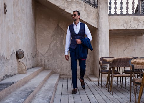 一位时尚男子穿着时髦服装，戴着太阳镜，披着西装外套在迪拜的户外行走