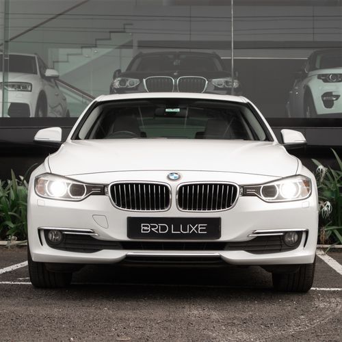 Free Front view of a white luxury BMW car with headlights on, parked outdoors. Stock Photo