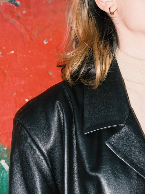 Free Stylish close-up of a woman in a black leather jacket with a vibrant red wall background. Stock Photo