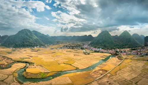 Free A picturesque rural landscape with rolling fields, mountains, and a river under a cloudy sky. Stock Photo