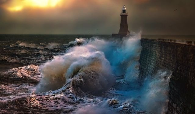 Waves breaking against a harbour wall by a lighthouse — photo by Ray Bilcliff on Pexels
