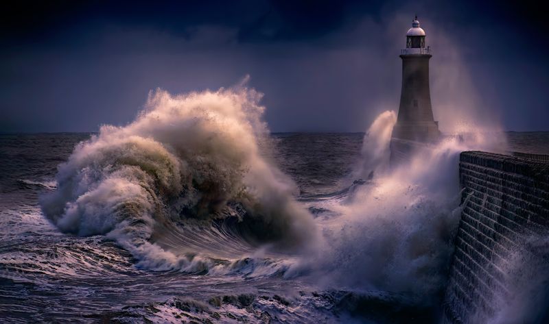 Storm waves breaking over a coastal lighthouse at night — photo by Ray Bilcliff on Pexels