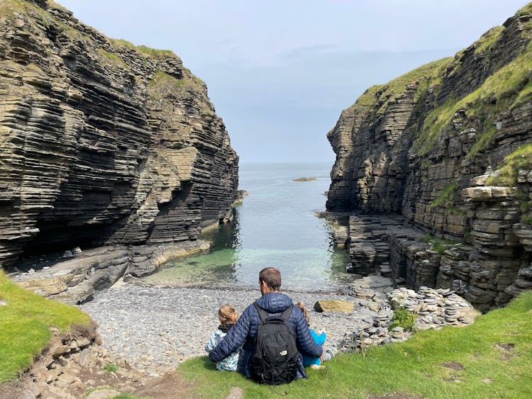 Father With Children Sitting In Bay Near Cliffs