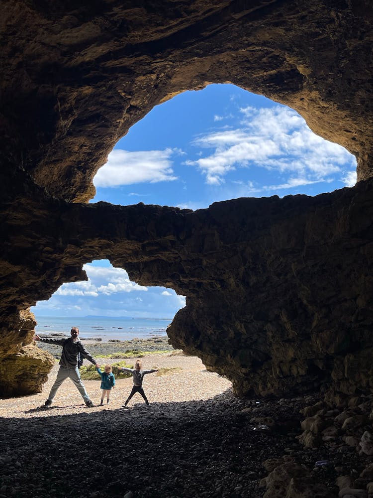 Father With Children Posing In Cave On Seashore