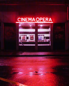 A moody night street scene capturing a neon-lit cinema in Lyon, France with wet reflections.