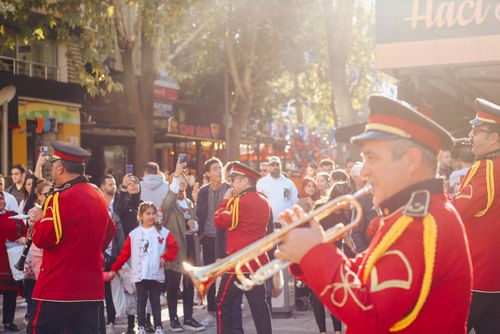 Free A vibrant street parade in Denizli features musicians in red uniforms playing instruments, surrounded by an excited crowd. Stock Photo