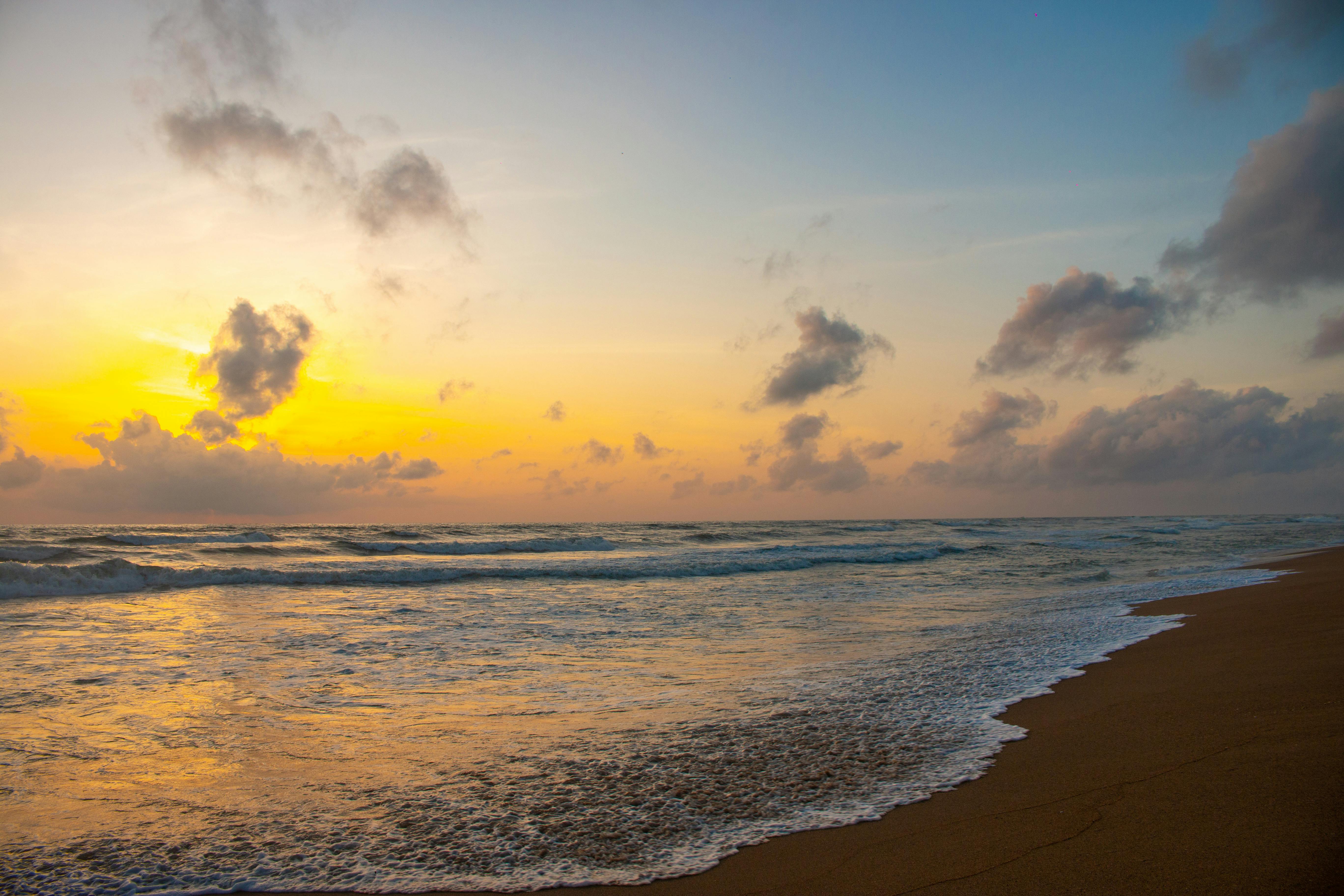 Serene beach at sunrise with golden and blue sky reflecting off waves.
