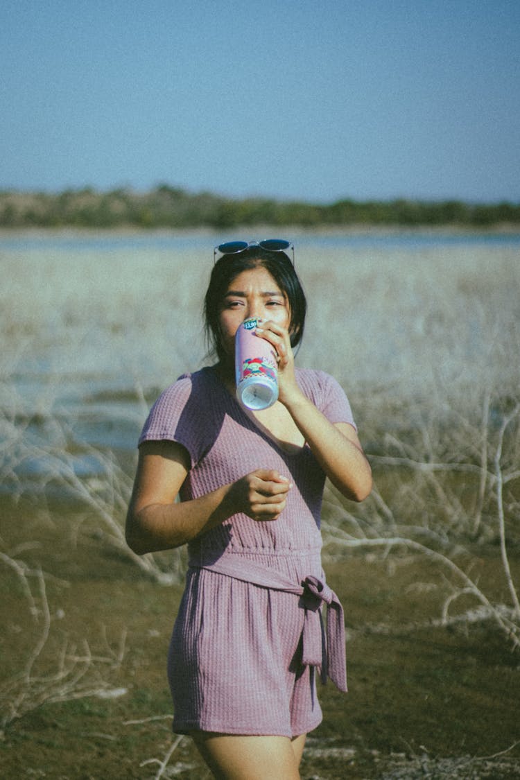 A Woman In A Jumpsuit Drinking From A Reusable Bottle