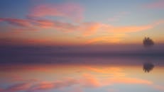 宁静的日出下，色彩缤纷的天空倒映在平静的海水和一棵孤树上