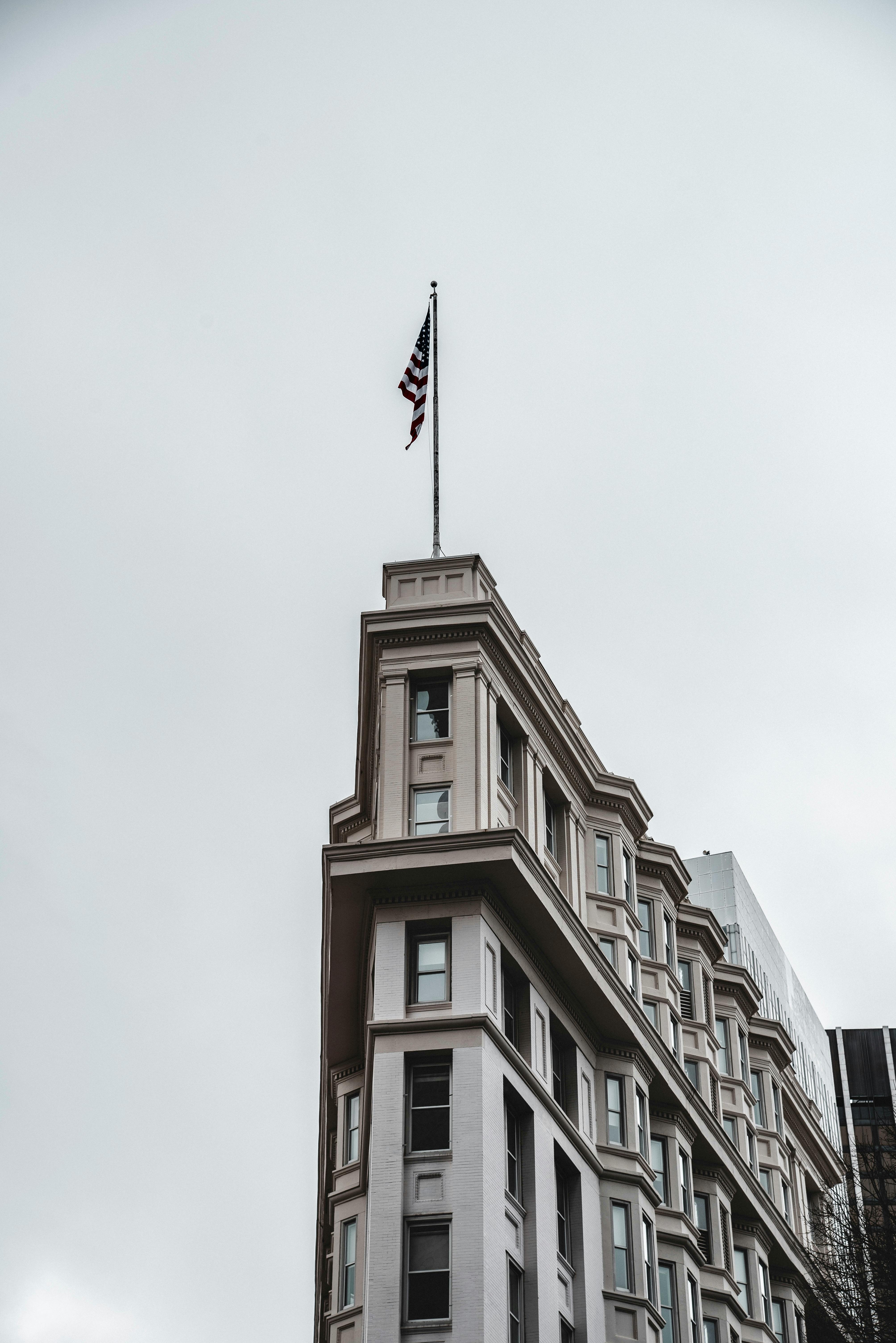 Free Architectural facade of a historic building featuring a USA flag under a cloudy sky in an urban area. Stock Photo