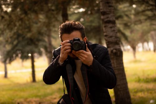 Free A focused photographer taking a picture in a wooded area using a DSLR camera. Stock Photo