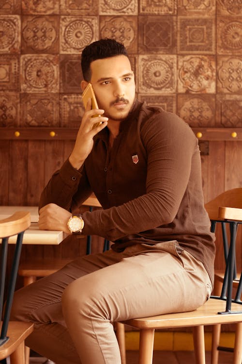 A Man in Brown Long Sleeves Sitting on the Chair while Talking on the Phone