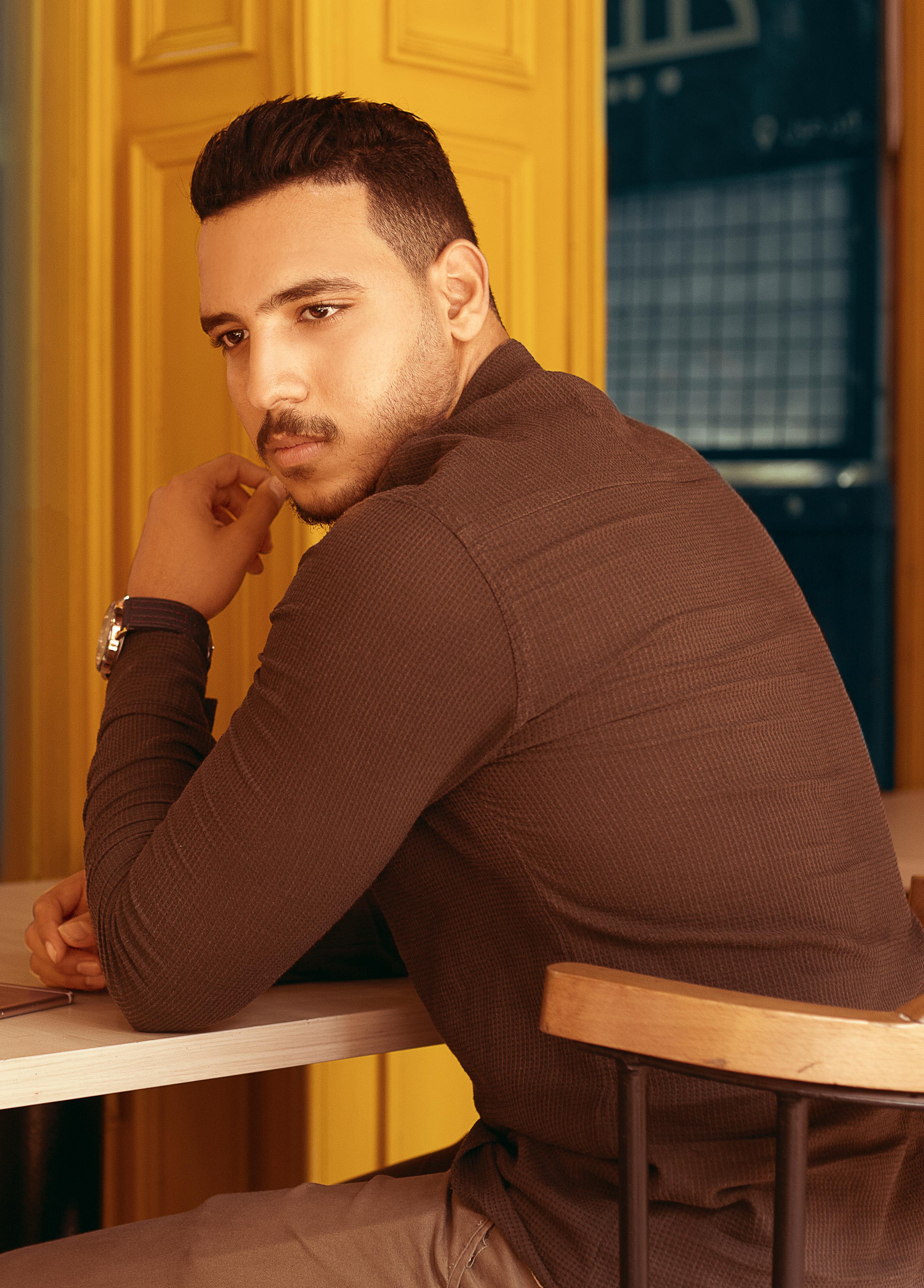 A man in a brown sweater sitting at a table in a stylish indoor setting.