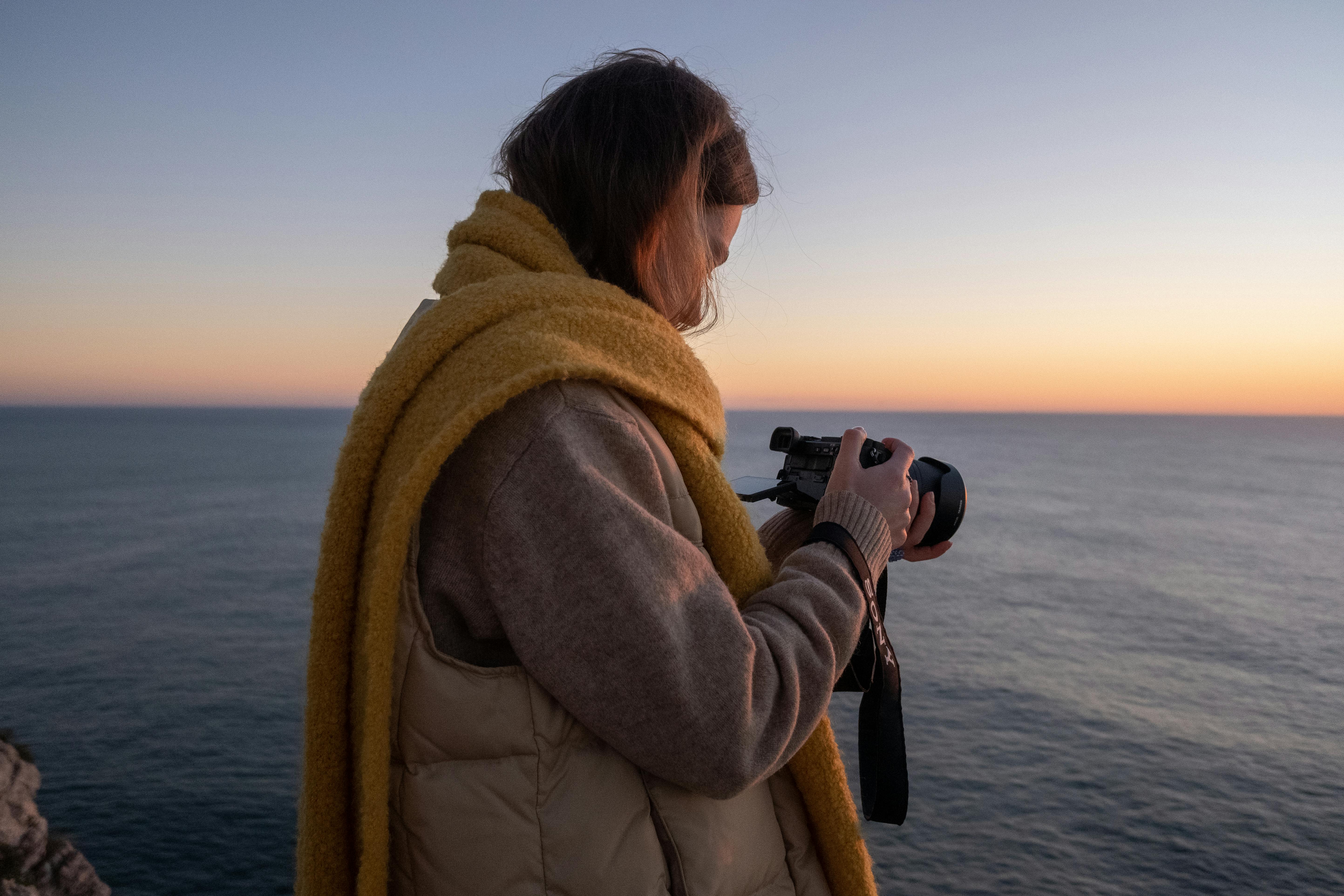 A woman with a camera takes photos of a serene ocean sunset.