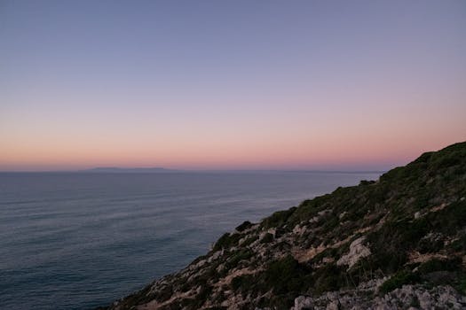 Peaceful sea view at sunset with pink sky and rocky cliff