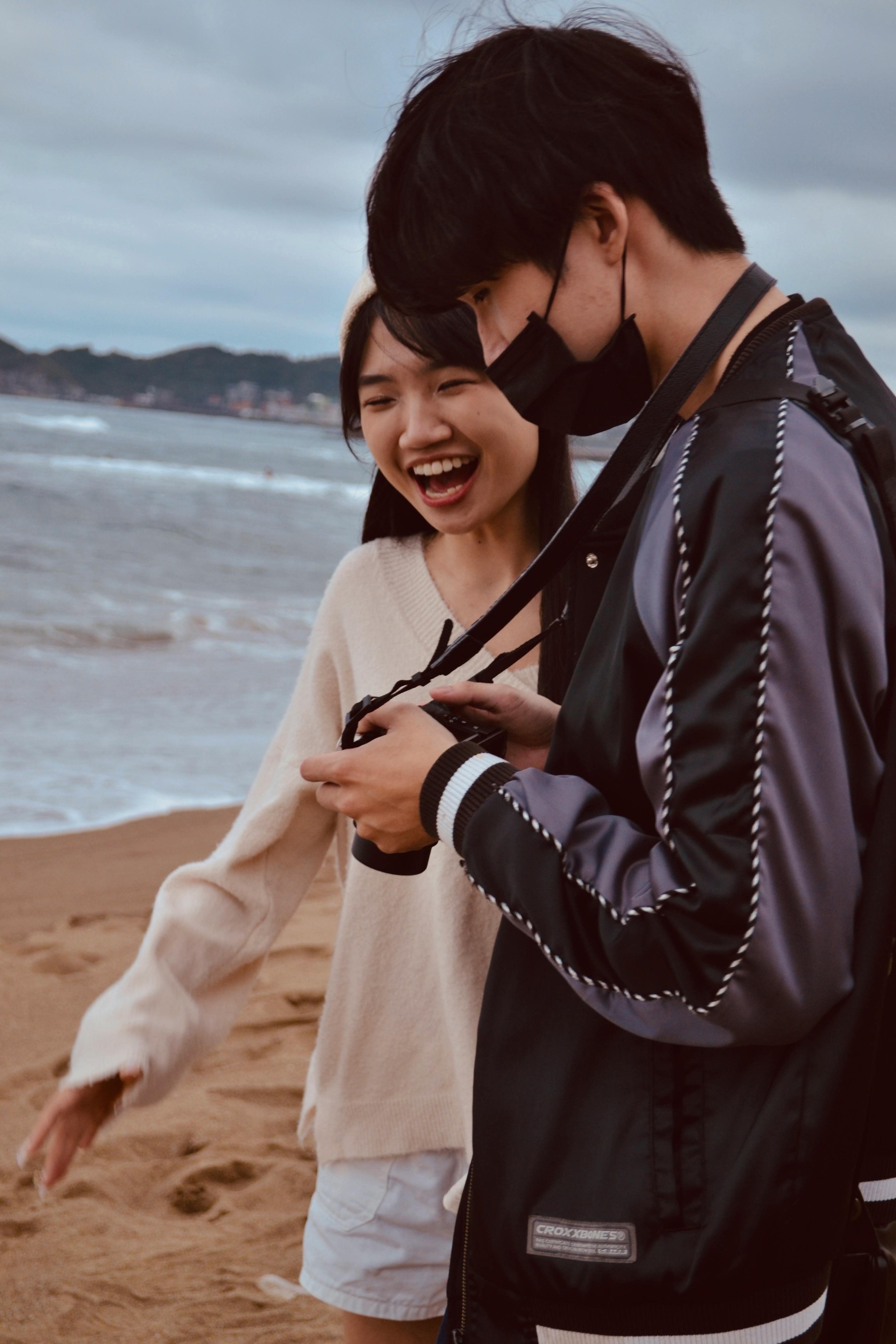 A joyful young couple laughing while reviewing photos on a beach.