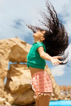 Energetic girl jumps freely by the beach, enjoying a sunlit day.