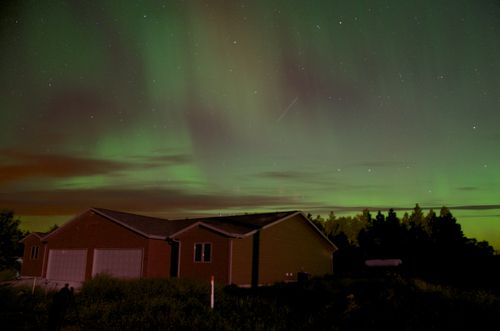 Free Scenic view of Northern Lights illuminating a house surrounded by nature at night. Stock Photo