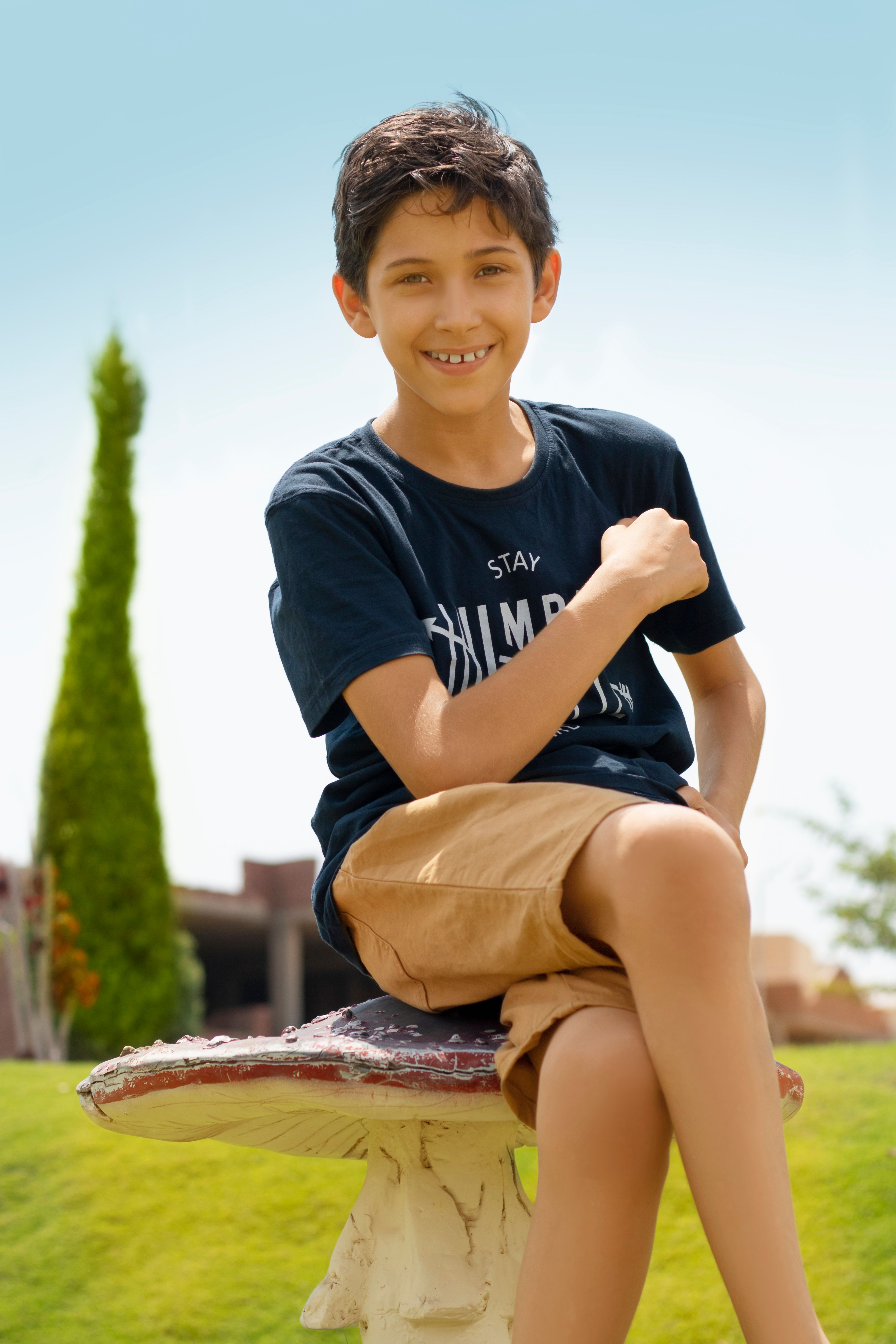 A cheerful boy sitting on a decorative mushroom seat in a sunny garden.
