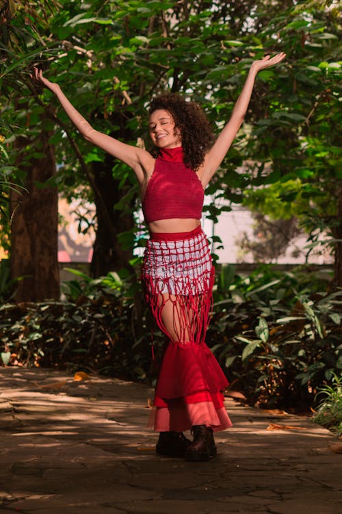 A Woman in Red Clothes Standing on the Street while Raising Her Hands