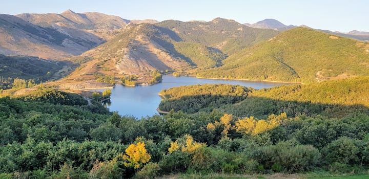在晴朗的天空下，美丽的山景和宁静的湖泊环绕着郁郁葱葱的绿色山丘