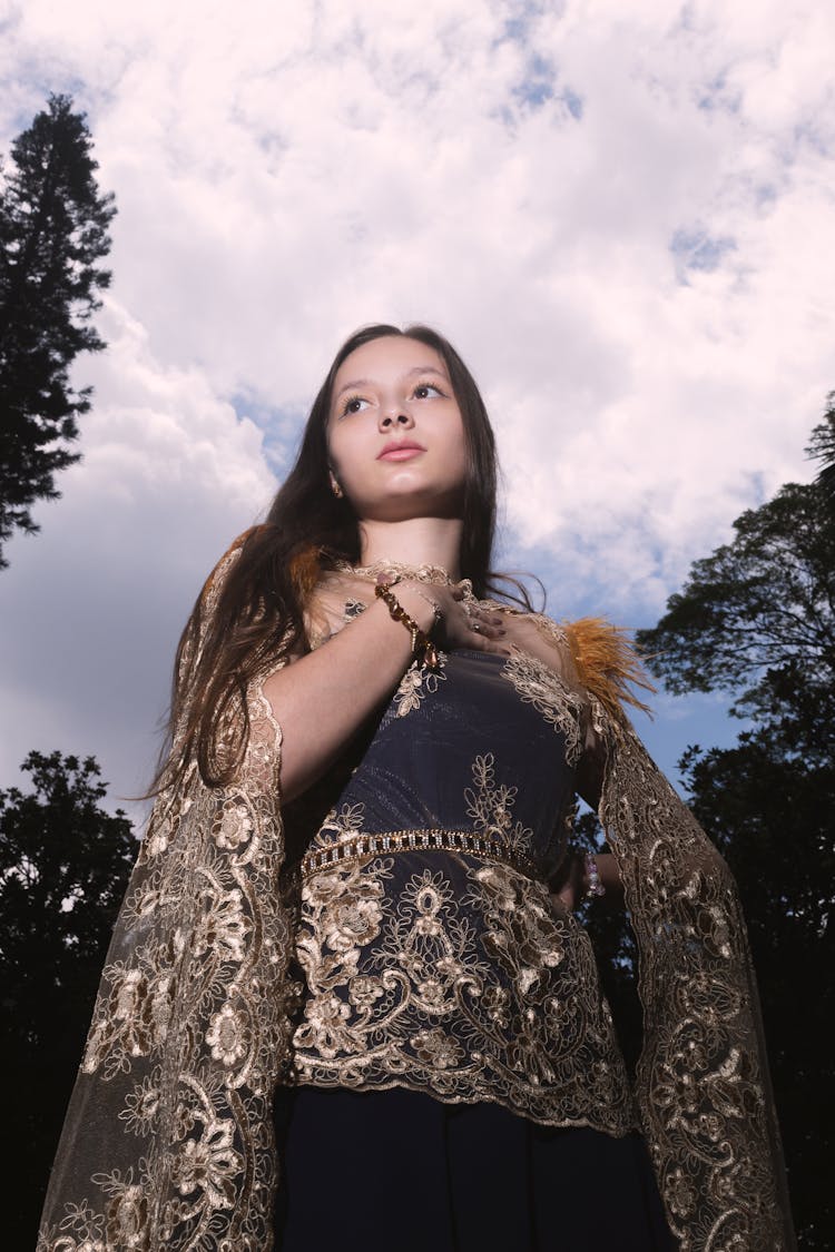 Low Angle Photo Of Woman In Golden Lace Dress Under Cloudy Sky