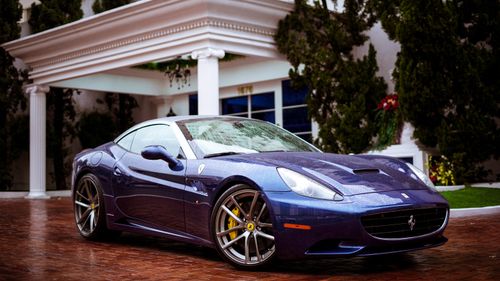 Free A sleek and shiny blue sports car parked outside a modern house with classical columns. Stock Photo