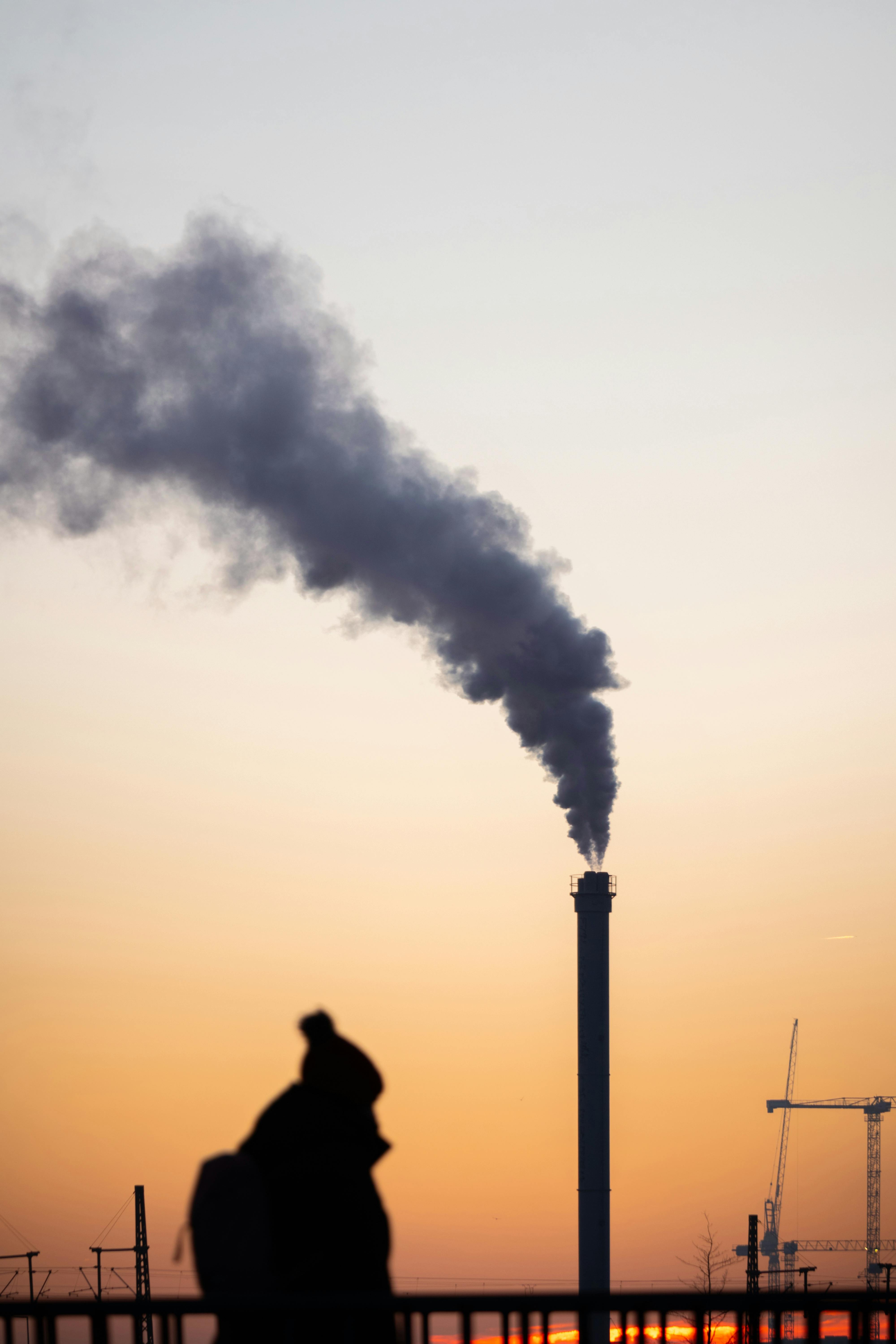 a person standing in front of a factory with smoke coming out of it