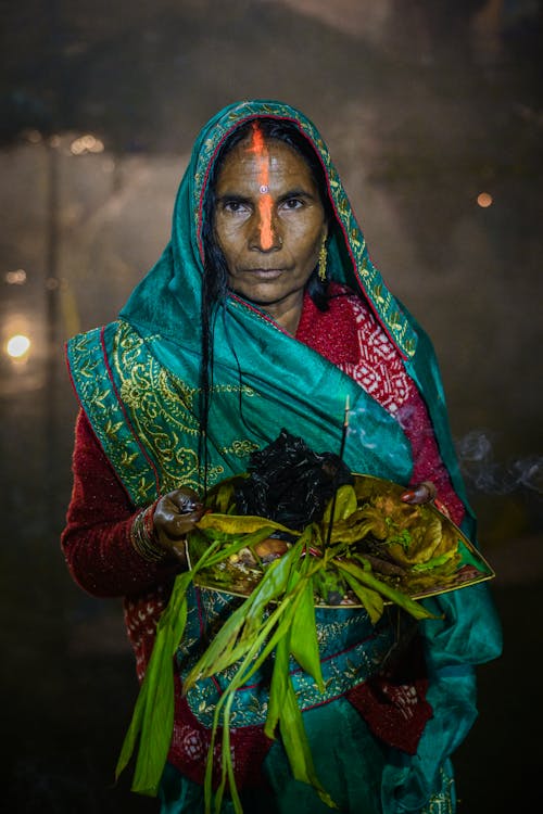 Elderly Woman in Traditional Clothing Standing Outside with Food in Her Hands