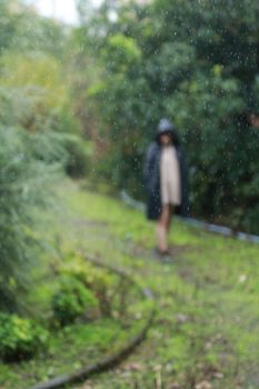 A woman in a raincoat walks in a lush Abbasabad park surrounded by greenery.