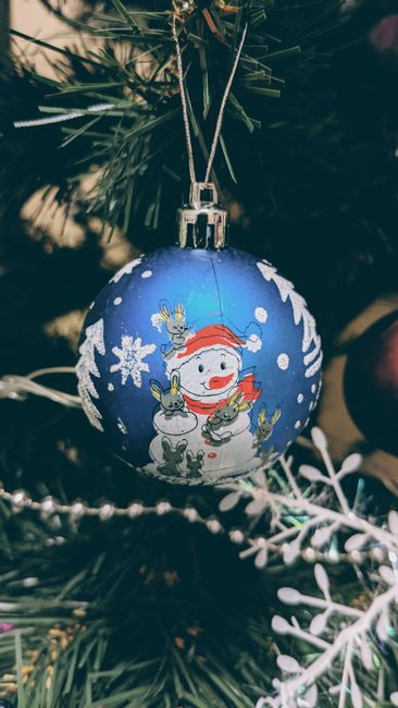 Close-up of festive blue Christmas bauble with snowman design and greenery.
