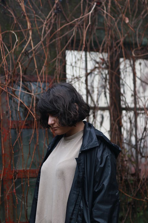 A Woman in Black Jacket Looking Down while Standing Near the Twigs