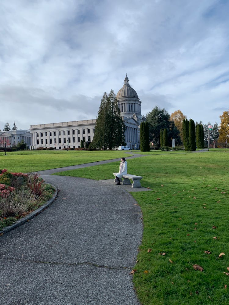 Woman Sitting On Bench In Park Surrounding Capitol