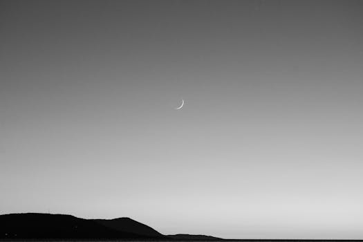 Black and white image of a crescent moon over a Podaca mountain landscape at twilight.