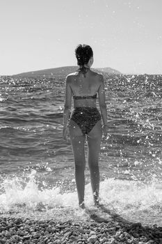 Monochrome image of woman in bikini standing by the ocean waves at Podaca, Croatia.