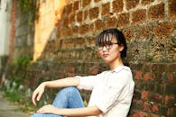 一位年轻女子身着休闲时尚的服装，靠在户外质朴的石墙上摆姿势