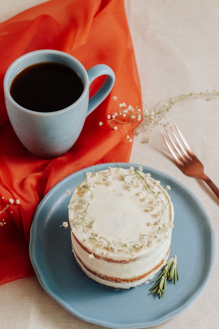 Studio Shot Of A Mug Of Coffee And White Cake With Edible Flowers On Top