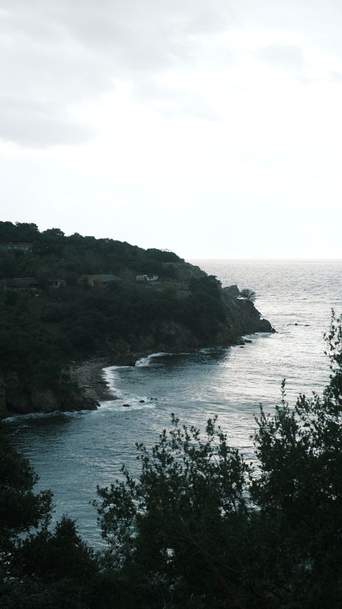 Free Serene coastal landscape featuring lush hills and a tranquil sea with scattered houses along the cliffside. Stock Photo