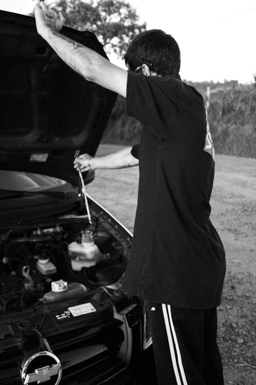 A Grayscale of a Man Opening the Hood of a Car
