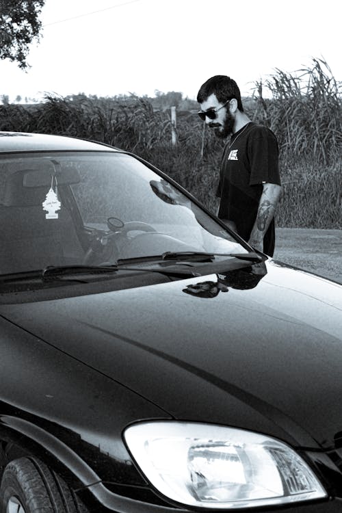 Black and White Photography of a Man Looking at His Car