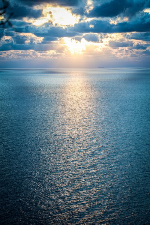 Free A stunning view of the ocean at sunset with dramatic clouds and shimmering water. Stock Photo