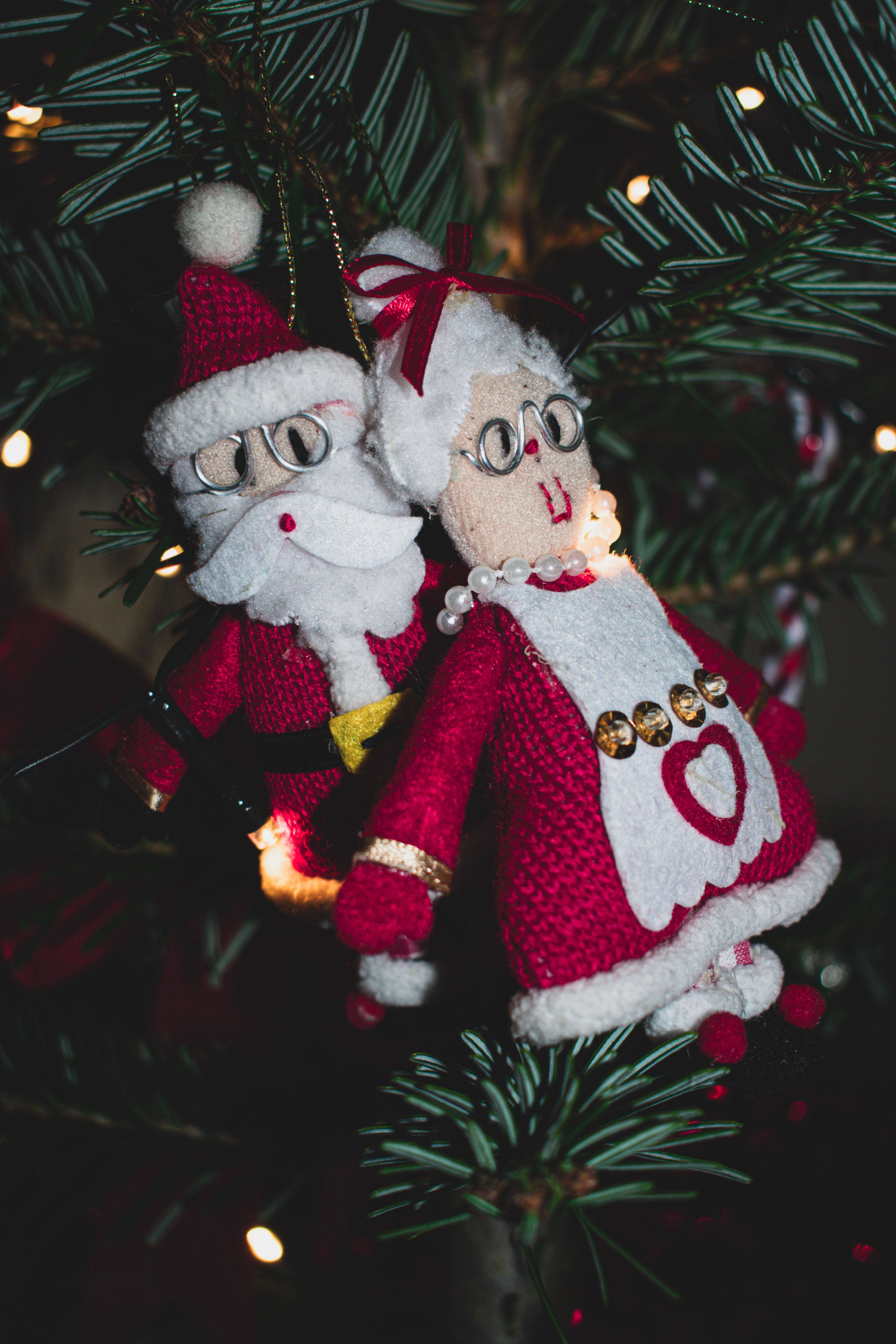 Festive Santa and Mrs. Claus ornaments hanging on a Christmas tree.