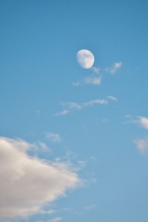 Free A serene view of the moon amidst a vibrant blue sky with scattered clouds. Stock Photo
